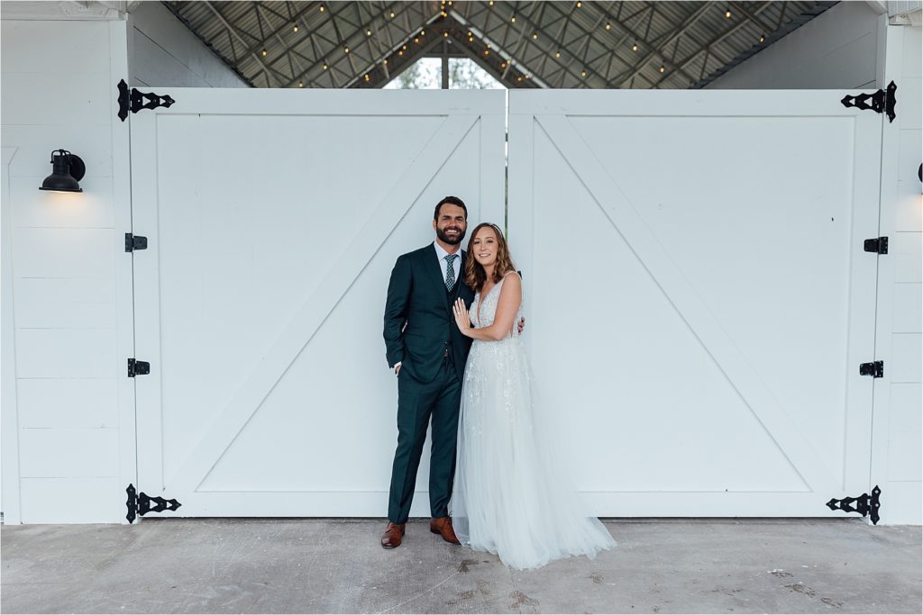 bride and groom standing together in front of barn doors